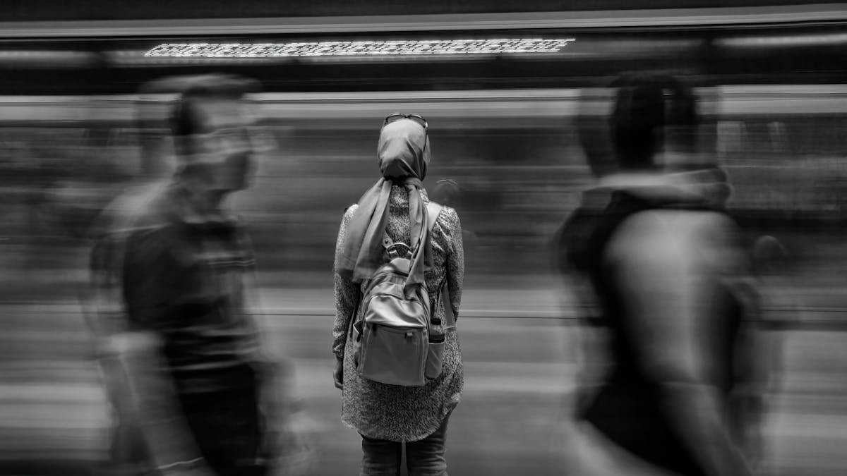 A woman in a busy subway station with motion blur of passing train.